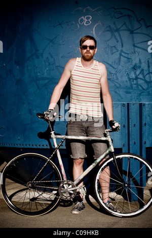 A fixed gear rider in a yellow striped tank top and sunglasses poses. Foto Stock