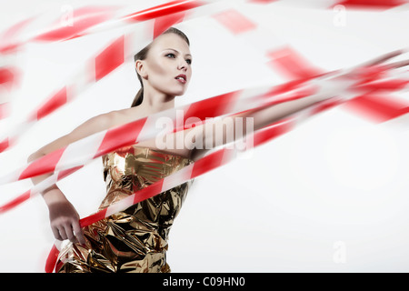 Giovane donna in un color oro lotte vestito attraverso lo sbandieramento del nastro barriera Foto Stock