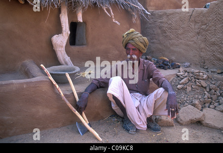 Il vecchio uomo che lavora nella parte anteriore della sua casa indossando un turbante e un dhoti, il tradizionale maschile di indumento, il Deserto di Thar, Rajasthan Foto Stock