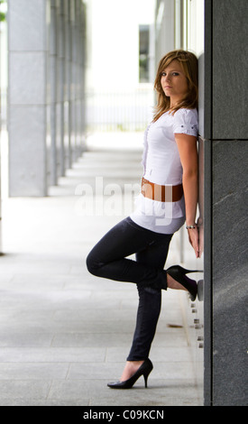 Giovane donna in piedi, appoggiata contro un muro di pietra Foto Stock