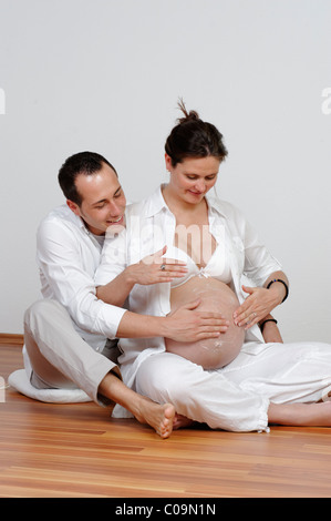 Donna incinta con partner che sta mettendo la crema sul suo ventre bambino Foto Stock