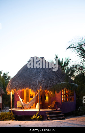 Una donna si siede in un'amaca sulla veranda della sua capanna di paglia presso un hotel di lusso in Belize. Foto Stock