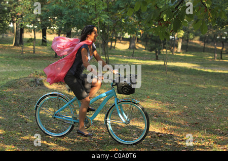 Immagine di un felice giovane donna con una sciarpa rosa in sella ad una bicicletta in un inizio autunno park. Foto Stock