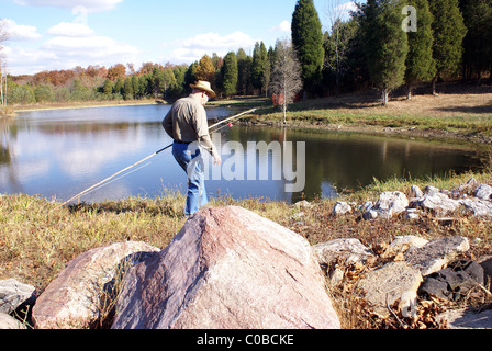 L'uomo cammina lungo il lago cercando per un perfetto luogo di pesca con canna pole. Foto Stock