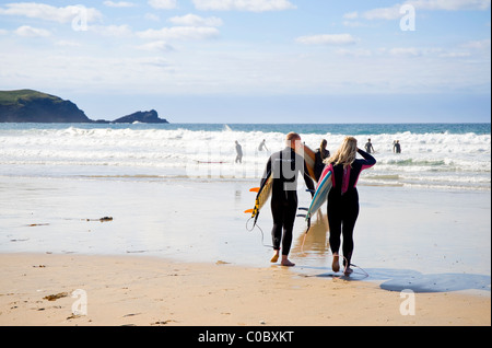 Newquay, Cornwall, England, Regno Unito - un giovane che trasportano le loro tavole da surf inserendo l'oceano a Fistral Bay, un posto popolare per surfer Foto Stock