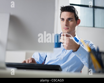 La metà degli adulti maschi caucasici business man guardando lo schermo di computer e di azienda blu tazza di caffè. Foto Stock