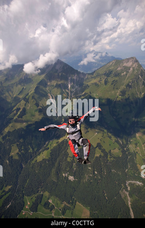 L uomo è il salto fuori da un piano all'interno di un sit posizione e volare attraverso il cielo blu sulle montagne. Foto Stock