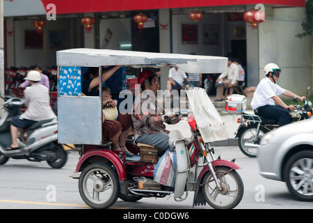 Scena di strada in Cina di un rickshaw driver con una donna e un bambino come passeggeri Foto Stock