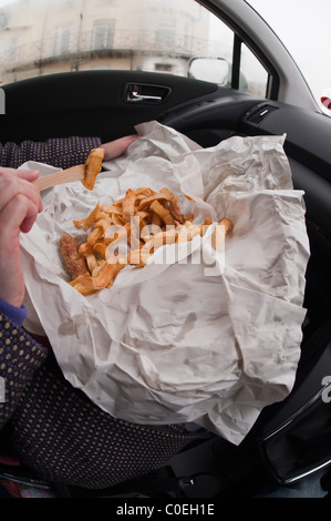 Una donna di mangiare pesce e patatine confezionate in carta all'interno di un automobile nel Regno Unito Foto Stock