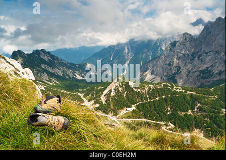 Vecchie scarpe da trekking sulle montagne sullo sfondo sotto il cielo nuvoloso Foto Stock