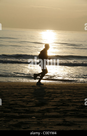 Uomo che corre sulla spiaggia con mare al tramonto Foto Stock