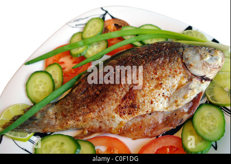 Pesce fritto il carassio su una piastra con i pomodori, i cetrioli, le cipolle e calce, è isolata, sfondo bianco Foto Stock