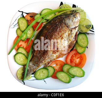 Pesce fritto il carassio su una piastra con i pomodori, i cetrioli, le cipolle e calce, è isolata, sfondo bianco