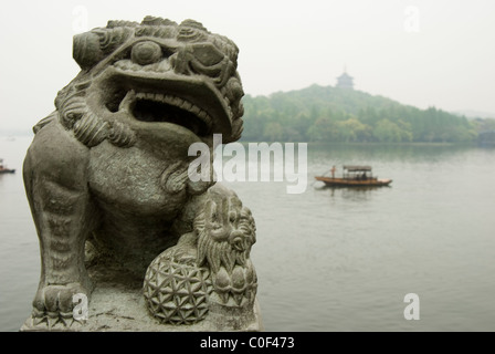 Statua di fu Leone accanto al Lago Ovest, Hang Zhou con Leifeng Tower e la barca in background. Foto Stock