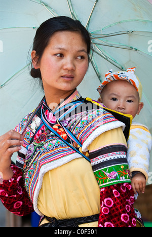 Asia, Cina Yunnan, Honghe Prefettura, Yuanyang County, Shengcun città. La minoranza Yi Donna con bambino in retro imbracatura e ombrello. Foto Stock