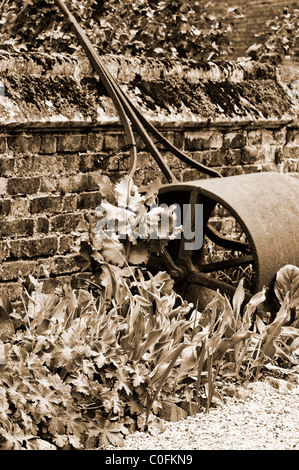 Il vecchio rullo da giardino appoggiata contro un muro di mattoni Foto Stock