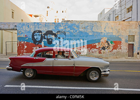 Un vecchio americano degli anni cinquanta la guida automobilistica passato un dipinto murale di Che Guevara in Havana Cuba Foto Stock