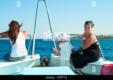 Due donne seduta sul ponte della barca in mare crociera e il piccolo bambino con loro Foto Stock