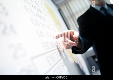 Un uomo presentando un foglio di calcolo di cifre su un interactive lavagna digitale presentazione powerpoint una riunione di affari, REGNO UNITO Foto Stock