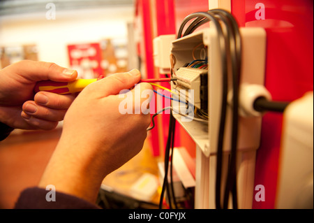 Un elettricista esperto al lavoro lavorare l'installazione di un sistema di distribuzione di elettricità in un negozio della fabbrica di office business UK Foto Stock