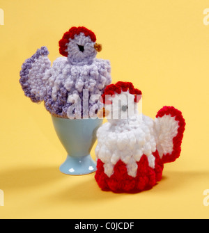Due graziosi in maglia di gallina uova di Pasqua scaldabiberon con uovo blu Cup su sfondo giallo. Foto Stock