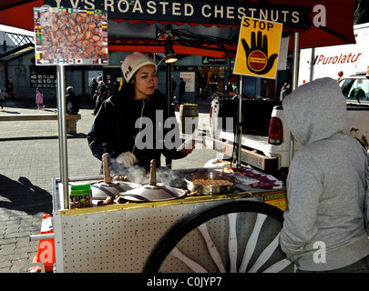 Giovane donna calda vendita Castagne Pistacchi dal carrello in ingresso al Granville Island Mercato Pubblico di Vancouver Foto Stock