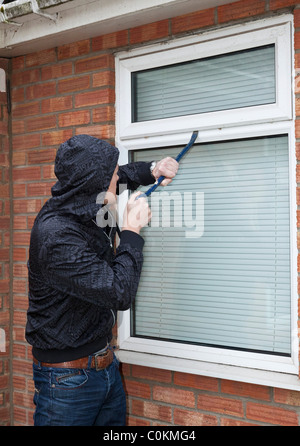 Un uomo che cerca di forzare una finestra su una casa Foto Stock