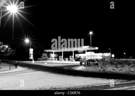 Una stazione di benzina nei pressi di una rotatoria su una coperta di neve strada illuminata da luci di strada al buio. Foto Stock