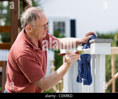 Senior uomo pittura un di legno decking recinzione Foto Stock