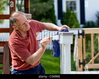 Senior uomo pittura un di legno decking recinzione Foto Stock