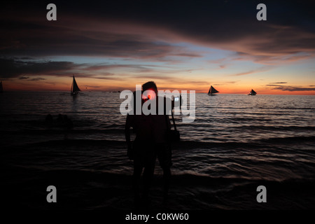 Turisti asiatici scattare un autoritratto durante il tramonto a spiaggia bianca, Boracay, Filippine. Foto Stock