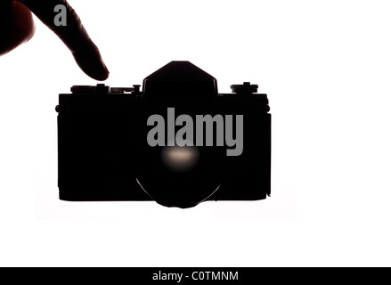 Il dito sopra il pulsante di scatto di una fotocamera reflex a obiettivo singolo su un bianco sfondo retroilluminato Foto Stock