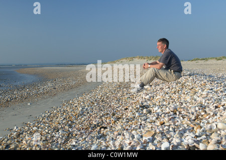 L'uomo persona seduta sulla ammassato gusci sul bordo occidentale della testata est, west wittering, west sussex, Regno Unito. settembre. Foto Stock