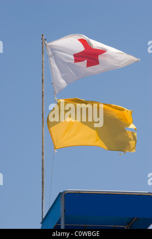 La Croce Rossa e le bandiere gialle su una spiaggia Foto Stock