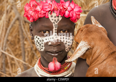 Karo ragazza con un archetto floreali, pitture facciali e una capra, Omo river valley, sud Etiopia Foto Stock
