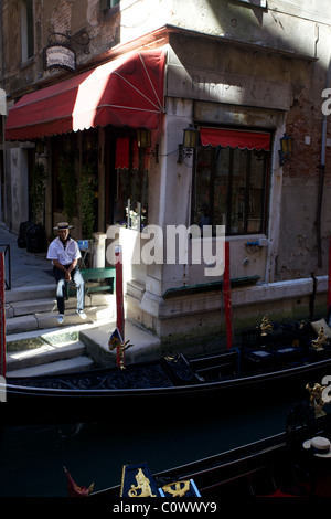 Un gondoliere siede in attesa di custom accanto alla sua gondola a Venezia Italia Foto Stock