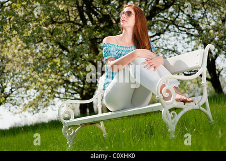 Capelli rossi donna a prendere il sole sul banco di bianco in un prato; shallow DOF Foto Stock