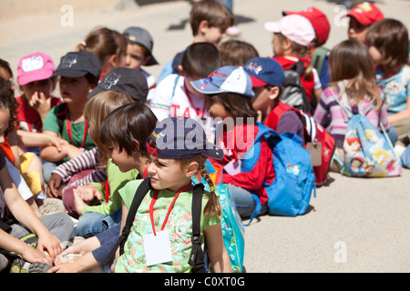 Gruppo di bambini seduti sul marciapiede durante il viaggio scolastico. Barcellona Spagna. Foto Stock