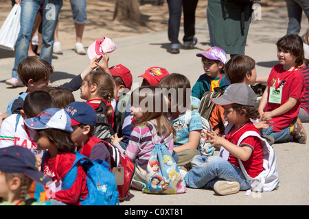 Gruppo di bambini seduti sul marciapiede durante il viaggio scolastico. Barcellona Spagna. Foto Stock