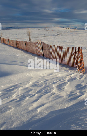 Capesante ruvida in deviati neve alla fine di una recinzione e derive liscia dietro il recinto di neve mostra il suo impatto sui modelli di vento. Foto Stock