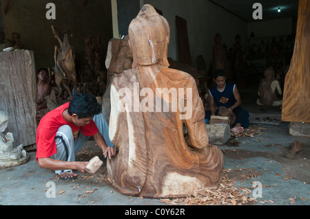 Un Balinese artigiano scultore in legno a lavorare su una scultura di un grande Buddha seduto nel villaggio di Peliatan Foto Stock