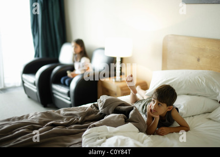 Ragazzo sul letto e ragazza di sedia, guardando montato a parete tv in una stanza del motel. Foto Stock