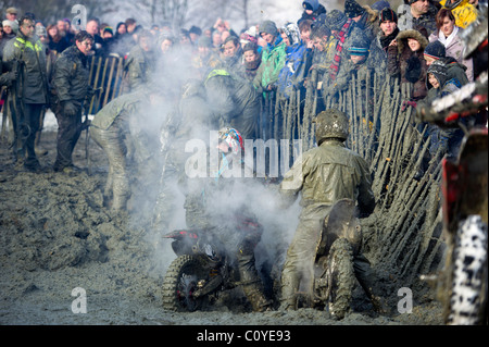 Uomo sulla fangosa motocross moto scrambling tirato da corda e il team di collaboratori al di fuori del foro di fango bog con vapore in aumento Foto Stock