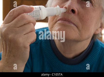 Close up donna anziana utilizzando uno spray nasale per alleviare i sintomi del raffreddore da fieno Foto Stock