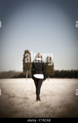 Una ragazza adolescente stand in un campo di indossare collant nero e un mantello nero con due alberi in lontananza. Foto Stock