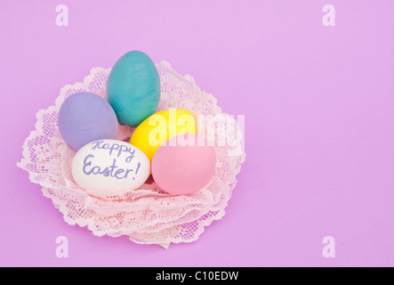 Dipinto a mano di colore pastello di uova di Pasqua in un nido fatto di pizzo rosa su sfondo viola chiaro, con spazio di copia Foto Stock