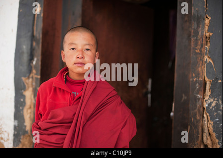 Giovane e orgoglioso monaco bhutanesi in piedi in un portale di un tempio nelle zone rurali del Bhutan Foto Stock