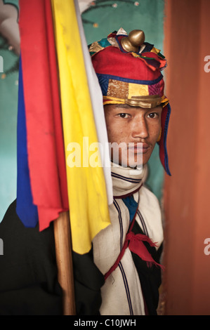 Bhutanesi uomo vestito in costumi colorati protezioni l ingresso del Punakha Dzong durante un grande festival e detiene un banner. Foto Stock