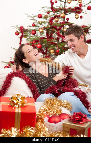 Sorridente coppia giovane seduti insieme nella parte anteriore dell albero di Natale Foto Stock