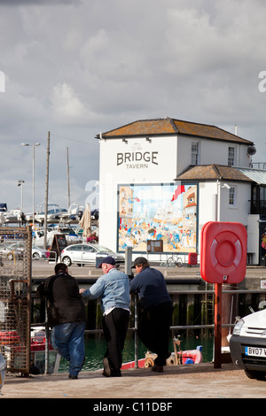 I pescatori chat su procedure Dockside Wizard nel Dock di camber con il ponte storico taverna in background. Foto Stock